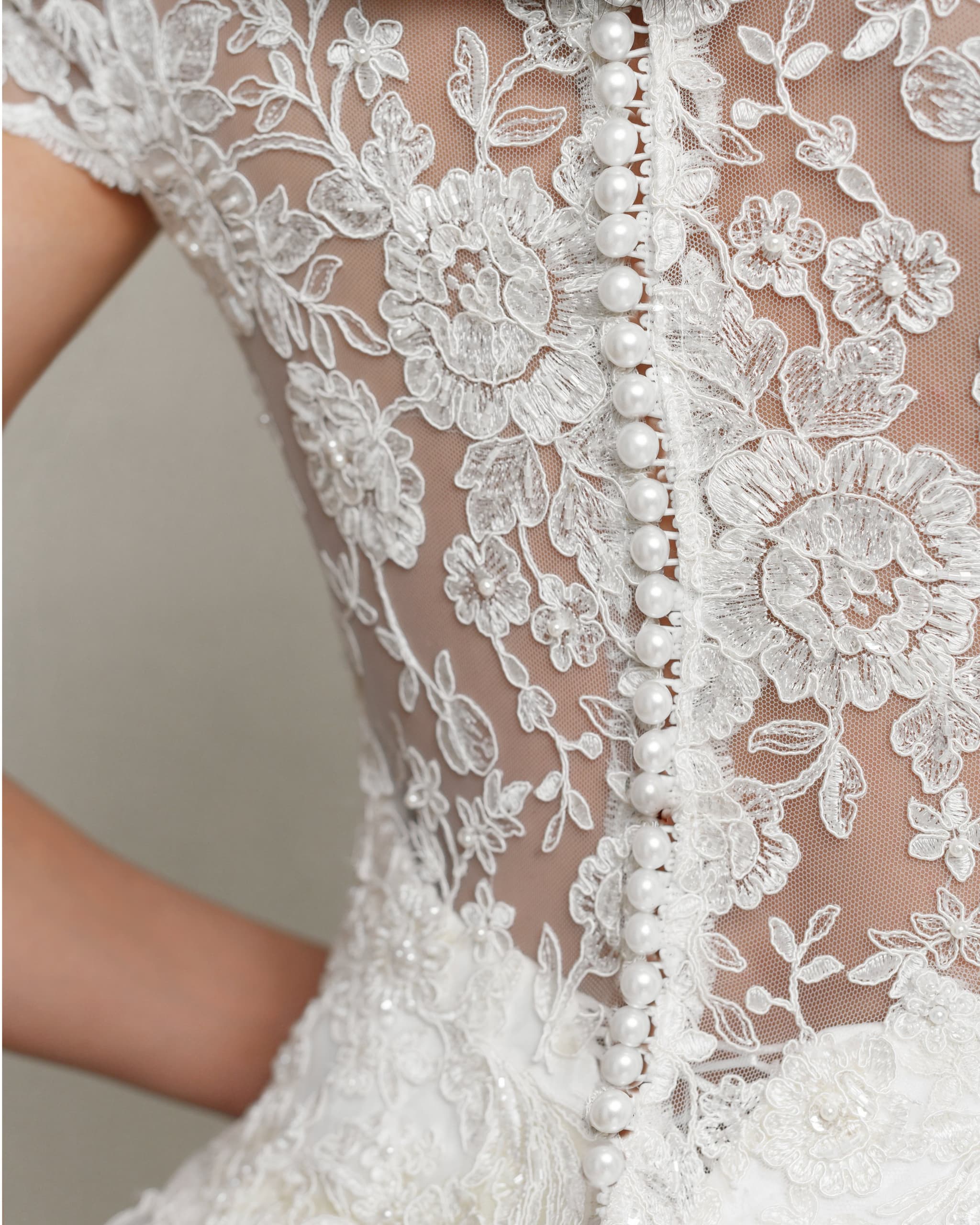 Elegantes weißes Brautkleid mit floralen Spitzenstickereien und perlmutternen Knöpfen, Detail-Aufnahme der Rückseite