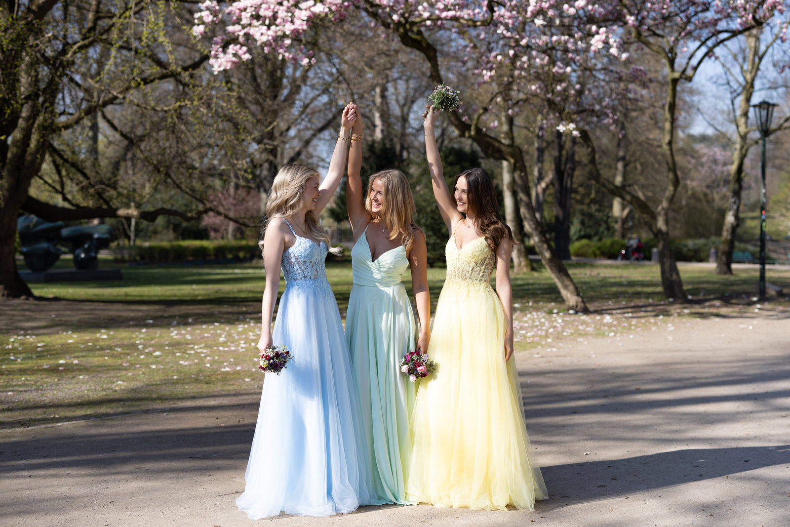 Drei junge Frauen in pastellfarbenen Ballkleidern unter Kirschblüten